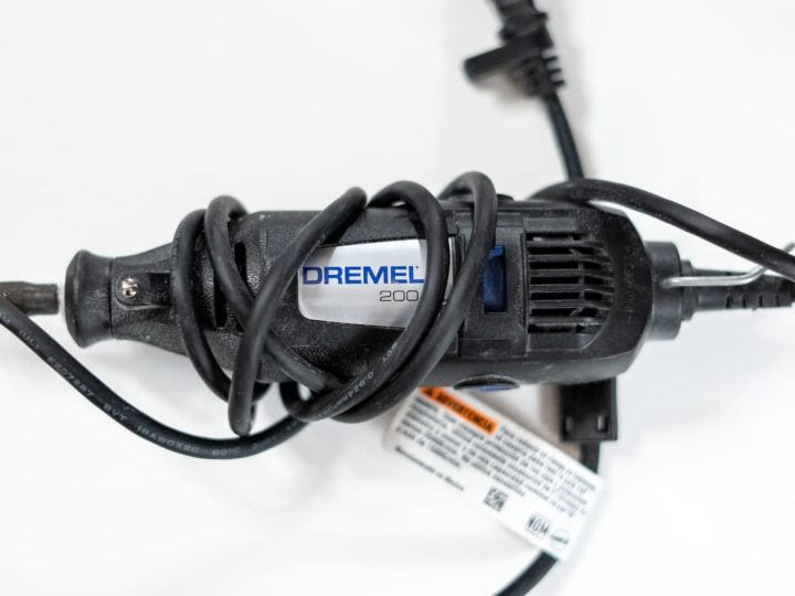 A black corded Dremel tool with the cord wrapped around the handle on a white background.