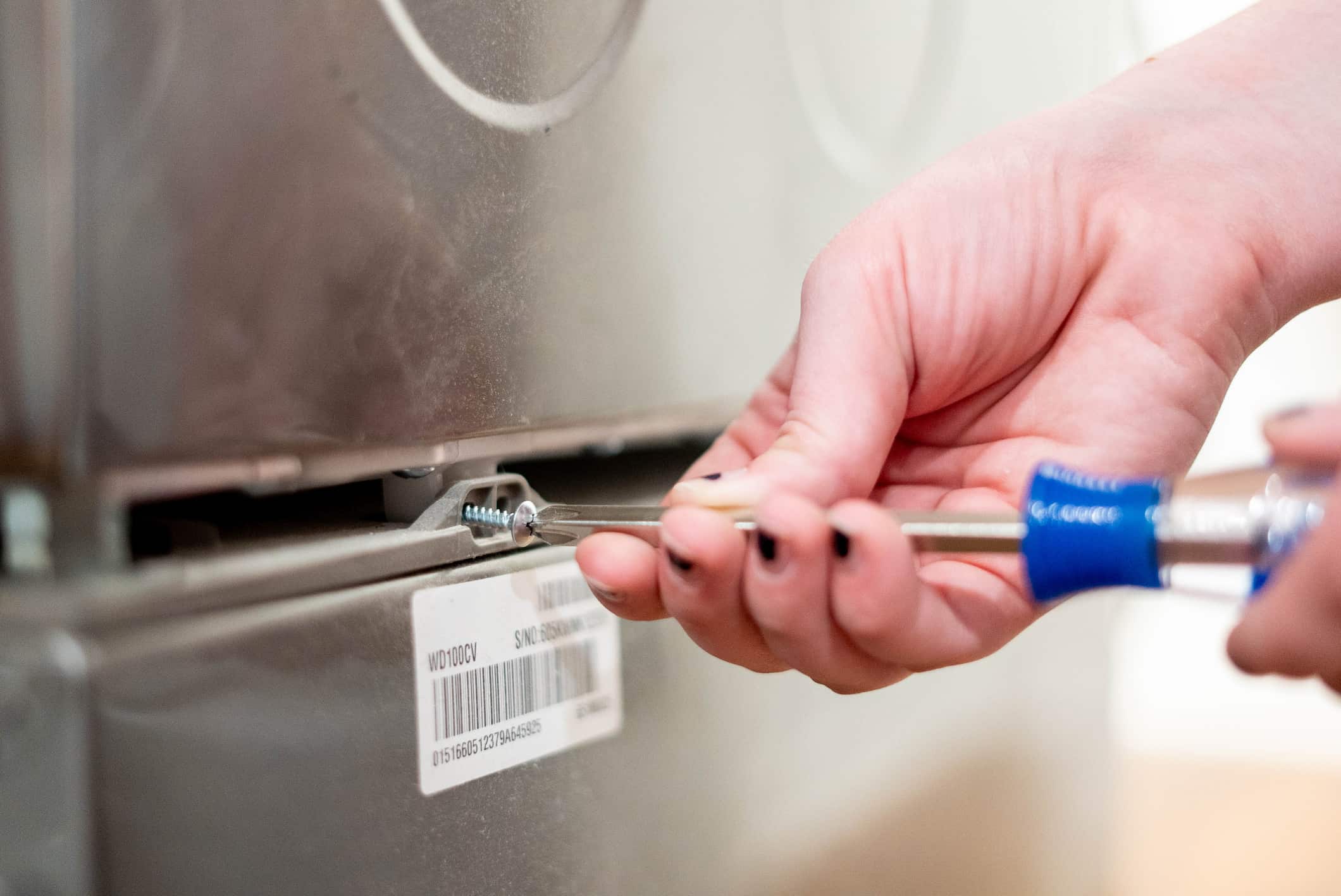 A woman unscrewing the clamp to illustrate how to remove the pedestal from a washer and dryer