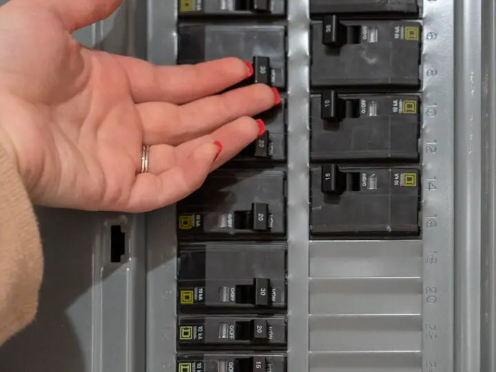 woman placing back of left index finger on circuit breaker to check its temperature
