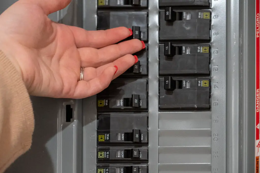 A woman testing the temperature of a circuit breaker to answer the question 'Should circuit breakers be warm?'